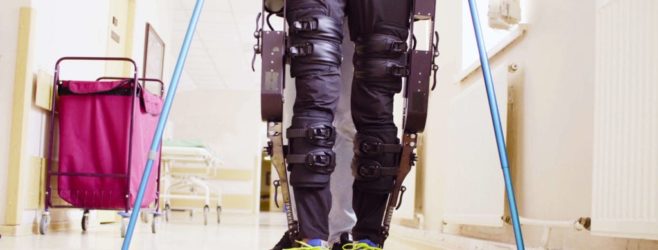 A man with a robotic exoskeleton on his legs walks down a hallway