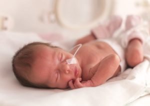 A newborn with hypoxic-ischemic encephalopathy sleeps in a hospital crib with a small plastic tube in their nose.