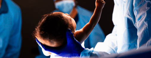 A doctor holds a newborn baby immediately after delivery in an operating room.