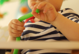 A young child in a striped shirt holding and bending a green flexible tube-shaped toy with both hands.