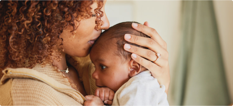 A mother holding a baby kisses their forehead.