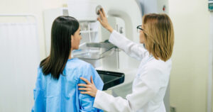 Woman standing in front of a mammography machine with her doctor. 