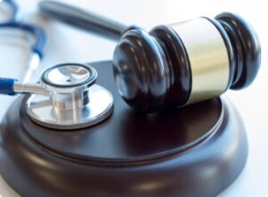 A gavel and stethoscope placed side by side on a wooden sound block.