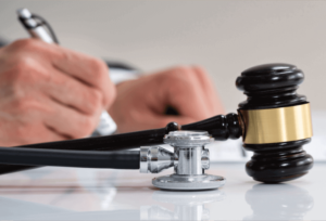 A hand writing with a gavel and stethoscope in the foreground to depict cerebral palsy lawsuit settlements.