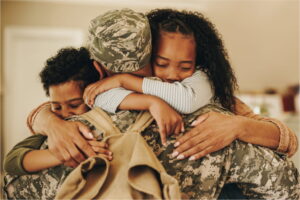 A person in military fatigues hugs two children