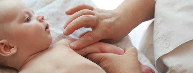A health care provider gently examines a baby's shoulder and arm during a medical exam.