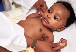 An infant lies on their back as an adult gently holds their arms during an examination.