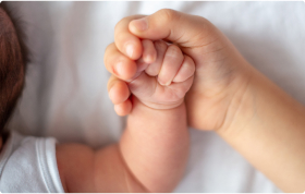 A close-up of a baby’s hand being gently held by an adult’s hand.