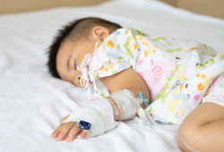 A young child sleeping in a hospital bed with an IV inserted into his arm.