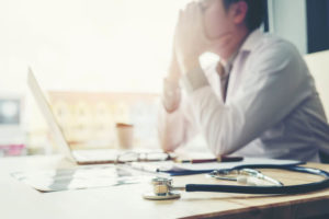 Doctor sitting at his desk with his held held down in his hands