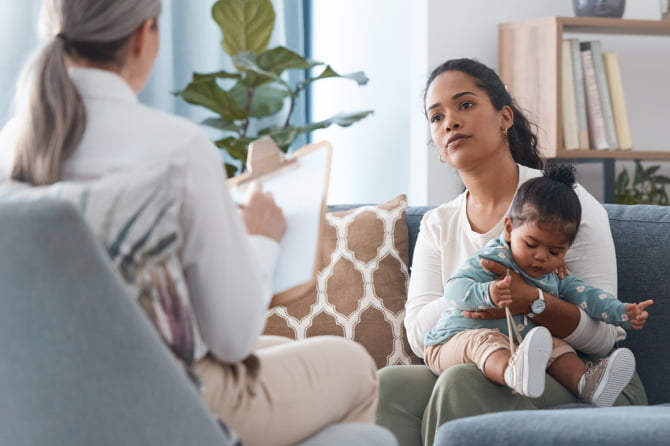 A young mother with her toddler looks worried as she talks to a financial planner holding a clipboard.