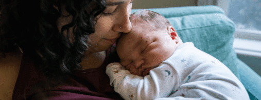 A mother holds a sleeping newborn close to her chest.