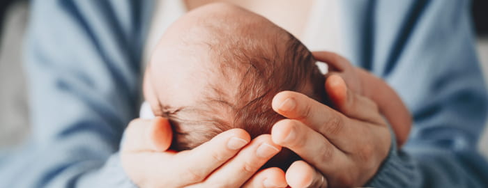 A delivery doctor cradles a newborn's head in their hands.