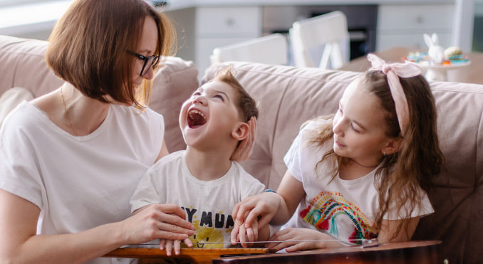 A mother and her young son with special needs laugh as his older sister shows him how to play the guitar.