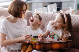 A mother and daughter help the sibling with special needs play a guitar.