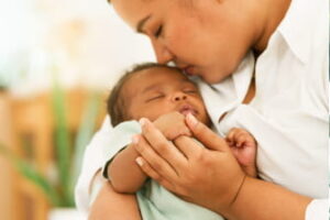 A mother cradles her sleeping newborn as the baby grasps her finger.