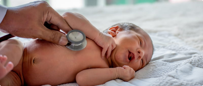 A doctor uses a stethoscope on a newborn to listen for breathing troubles that could be meconium aspiration syndrome symptoms.