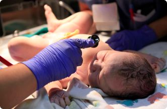 A medical professional examines a newborn in a hospital bed, shining a light in the baby’s eyes.