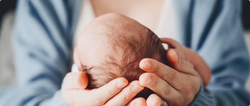 A delivery doctor cradles a newborn's head to check for infant brain damage symptoms.