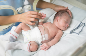 A newborn lying in an incubator with feeding and monitoring tubes, receiving care.