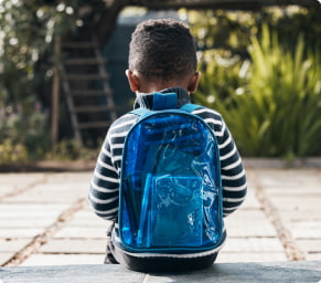 A young child wearing a backpack sits alone outdoors.