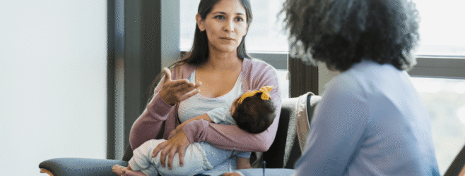 A mother holds her baby while speaking with a health care provider.