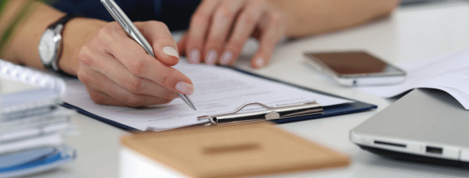A person reviews and takes notes on documents at a desk.