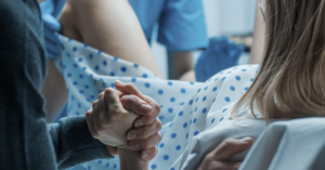 A mother gives birth in a delivery room while holding her partner's hand.