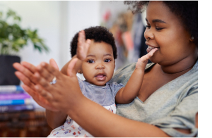 A mother holding her toddler while they clap hands together and smile.