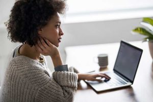 A woman working on a laptop with a puzzled expression.